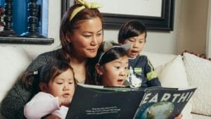 A mother and her three young children sitting on the sofa, reading a book together in honor of National Family Literacy Day.