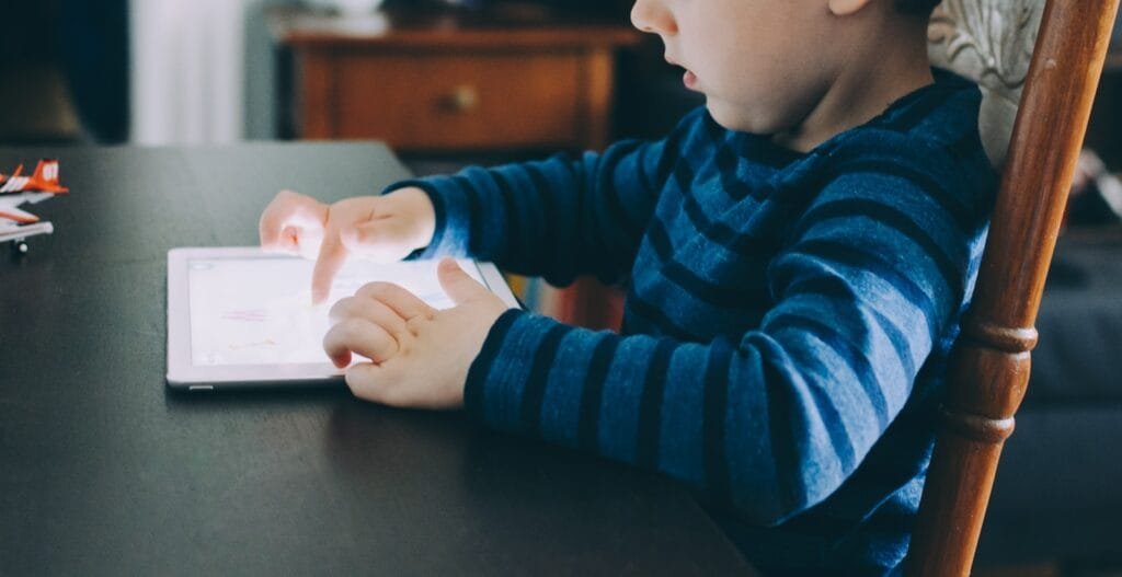 boy sitting on chair beside table using tablet computer reading living books